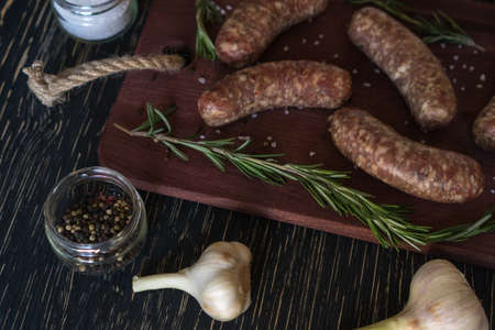 Raw sausages with garlic, rosemary on wooden surfaceの写真素材