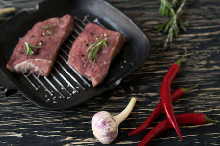 raw steak on cast iron frying pan with garlic and pepper.の写真素材