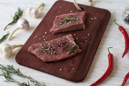 Fresh raw steaks with rosemary, pepper and garlic on wooden deskの写真素材