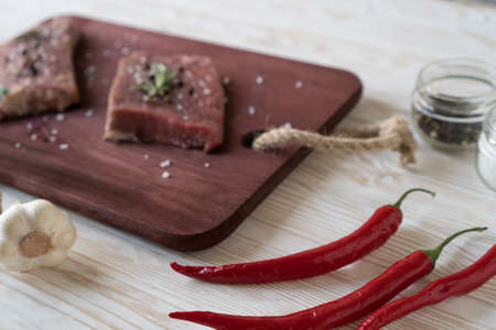 Fresh raw steaks with rosemary, pepper and garlic on wooden desk