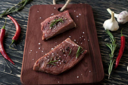 Fresh raw steaks with rosemary, pepper and garlic on wooden deskの写真素材