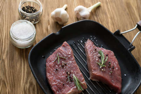 raw steak on cast iron frying pan with rosemary and garlic.の写真素材
