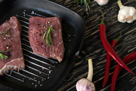 raw steak on cast iron frying pan with garlic and pepper.の写真素材