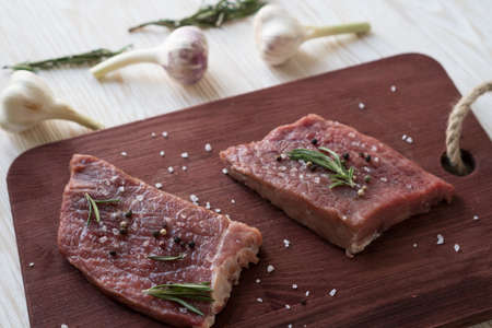 Fresh raw steaks with rosemary and garlic on wooden deskの写真素材