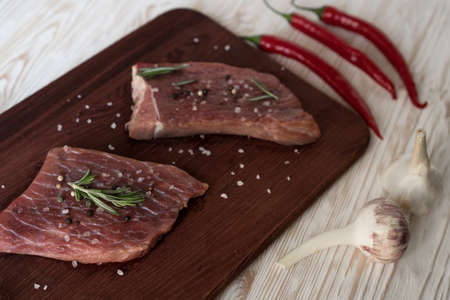 Fresh raw steaks with rosemary, pepper and garlic on wooden deskの写真素材