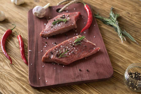 Fresh raw steaks with rosemary, pepper and garlic on wooden deskの写真素材