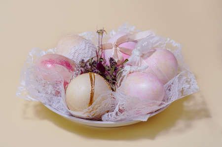 Dyed Easter eggs with lace on a plate on a yellow background