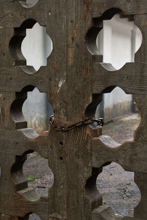 Fragment of a wooden gate with carved holes. The gate is closed with an iron chain.の写真素材
