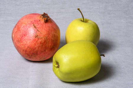 On a table covered with a gray tablecloth lie two yellow apples and a large red pomegranateの写真素材