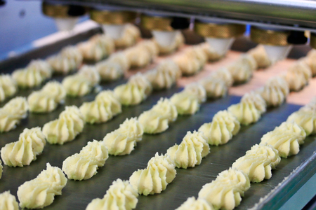 Automated biscuit cookies production process. Conveyor transfers the biscuits from the forming machine to the oven band.Selective focus.の写真素材