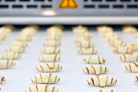 The process of producing croissants on an automatic industrial machine line. Selective focus.の写真素材