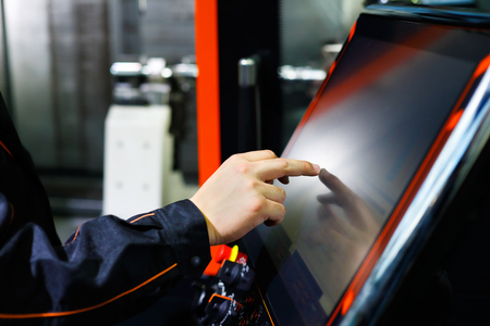 The operator adjusts modern CNC lathe machine using the touch screen. Selective focus.