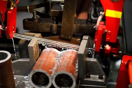Automatic band saw machine cutting metal pipes with coolant. Selective focus.