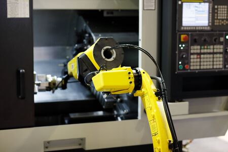 Robot arm is loading detail into CNC lathe machine. Selective focus.