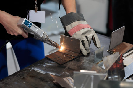 Young female welder working with handheld fiber laser welding machine. Selective focus.