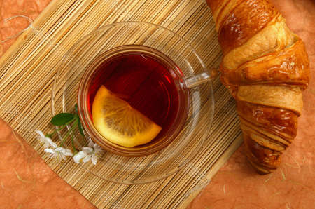 Tea with lemon and croissant on orange background.の写真素材