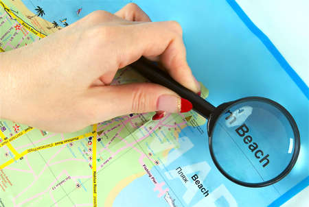 Close-up of woman’s hand holding a magnifying glass on the map. Concept of beach tourism