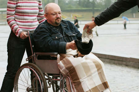 Young man in wheelchair takes a handout from the stranger.の写真素材