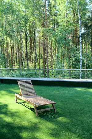 A wooden lounge chair on a green grass near a birchwoodの写真素材