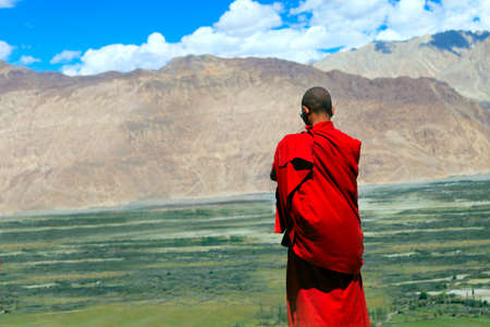 Buddhist monk looks at the Himalayas and valleyの写真素材