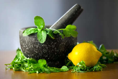 Herb leaf selection in a granite mortar with pestle with lemon on wooden tableの写真素材