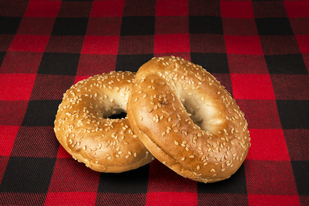 Fresh sesame seed bagel bread, isolated on a tartan red and black tablecloth in background.の写真素材