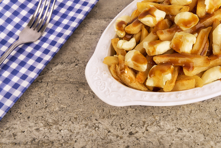 Poutine plate on a concrete background. Cooked with french fries, beef gravy and curd cheese. Canadian cuisine.の写真素材