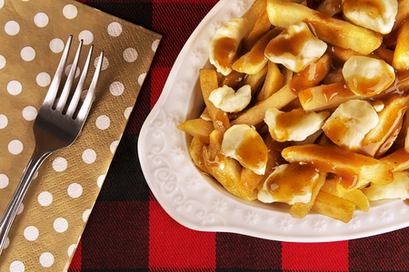 Poutine plate on a red and black tartan tablecloth. Meal cooked with french fries, beef gravy and...