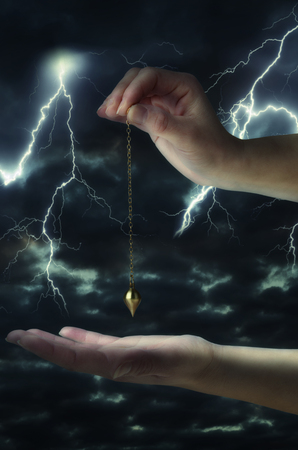 Close up of woman's hand holding a pendulum over her palm. Thunderstorm at night in background.の写真素材