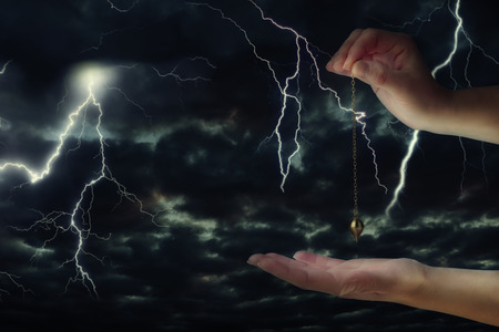Close up of woman's hand holding a pendulum over her palm. Thunderstorm at night in background.の写真素材