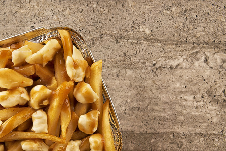 Poutine in a takeout container. Cooked with french fries, beef gravy and curd cheese. Copy space for...