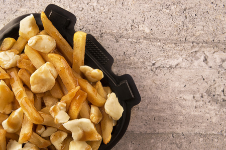 Poutine in a takeout container. Cooked with french fries, gravy and curd cheese. Canadian cuisine.