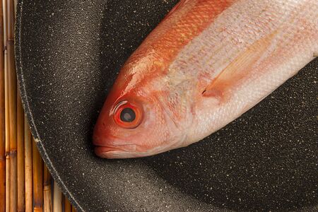 Red snapper raw fish isolated disposed in a fry pan. Bamboo table in background.
