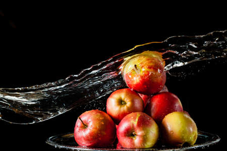 The few red apples lying on a silver top and falling water on a black backgroundの写真素材