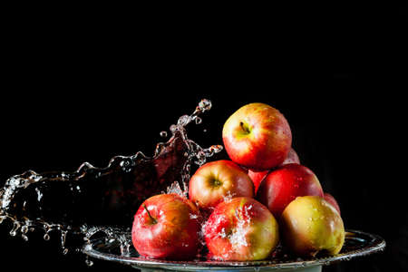 The few red apples lying on a silver top and falling water on a black backgroundの写真素材