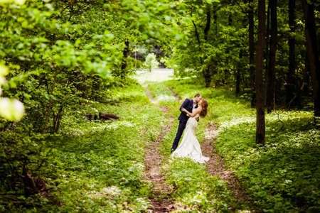 Bride and groom in the spring forest are kissing on a footpathの写真素材