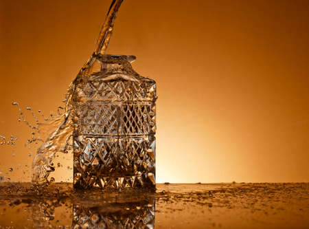 Decanter with an alcoholic beverage on a gold background, and liquid droplets flying in the airの写真素材