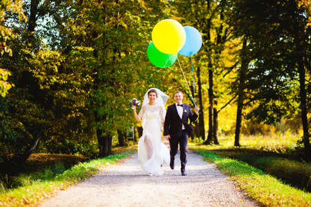 The bride and groom running through the alley with balloons on a background of yellow leaves of autumnの写真素材