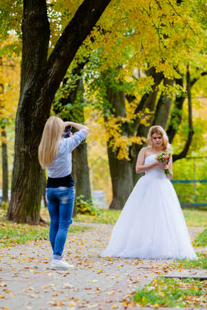 Wedding photographer is taking pictures the bride in the autumn parkの写真素材