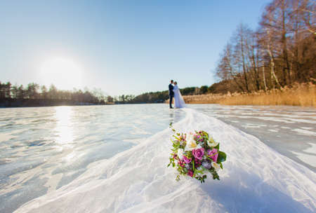 Bride and groom are standing at the surface of frozen lake with long bridal veilの写真素材