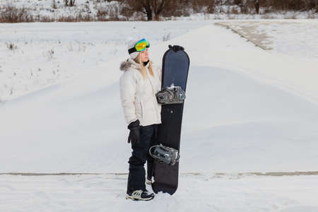 Young woman and her snowboard on snow-covered mountainside at sunsetの写真素材