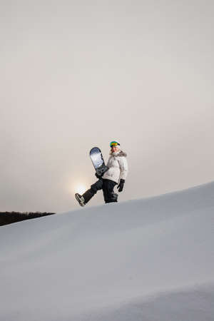 Young woman and her snowboard on snow-covered mountainside at sunsetの写真素材