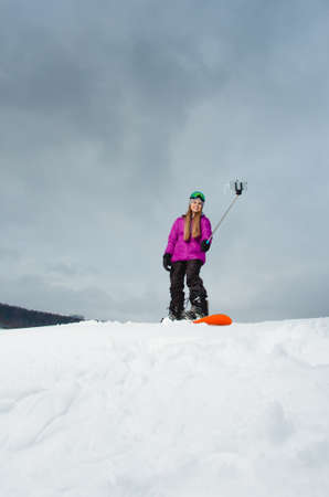 Young woman with the snowboard shooting a selfie by her cell phoneの写真素材