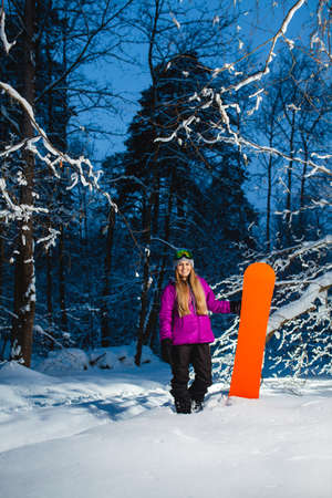 Young sexy woman with her snowboard in the dark winter forestの写真素材