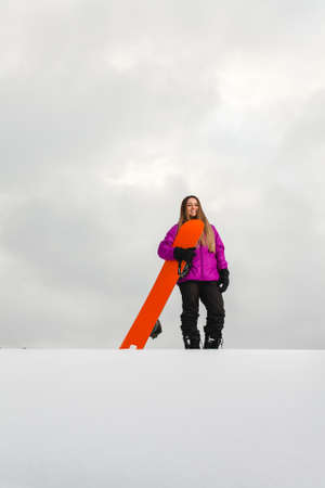 Young woman and her orange snowboard on a snow-covered mountainsideの写真素材