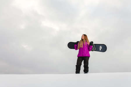 Young woman and her snowboard on a snow-covered mountainsideの写真素材