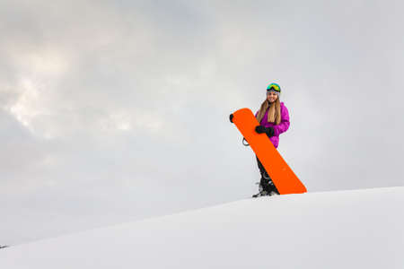 Young woman and her orange snowboard on a snow-covered mountainsideの写真素材