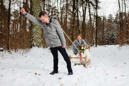 Groom and bride in the cold winter forest with the big wooden sledの写真素材