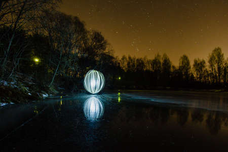 Futuristic glowing sphere on the surface of frozen lake at the background of spring night landscapeの写真素材