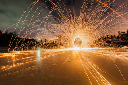 Trajectories of burning sparks on the surface of frozen lake at the background of spring night landscapeの写真素材